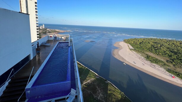 A high-rise building with a rooftop pool overlooking a beach and ocean. - Luxury Apartment with Voice Automation (Barra de Jangada Jaboatão dos Guararapes)