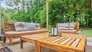 A wooden bench with cushions and a table in a garden setting. - Cozy 2BR Retreat + BBQ, WIFI & Parking (Raleigh)