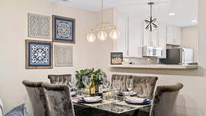A dining area with a glass table, cushioned chairs, and a chandelier. - Cozy 2BR Retreat + BBQ, WIFI & Parking (Raleigh)