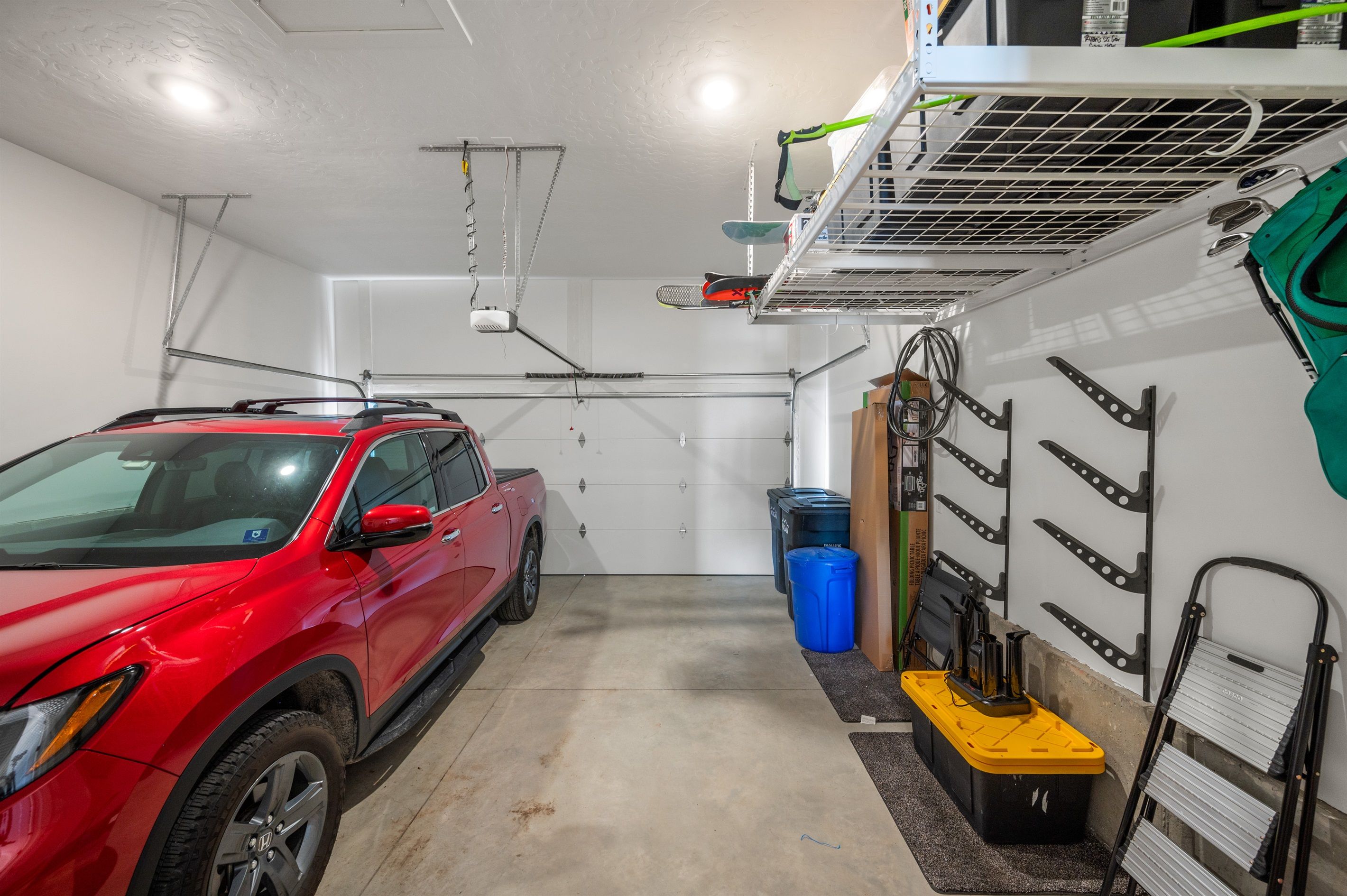 A garage with a red SUV parked inside, a white door, and a ventilation system on the ceiling.