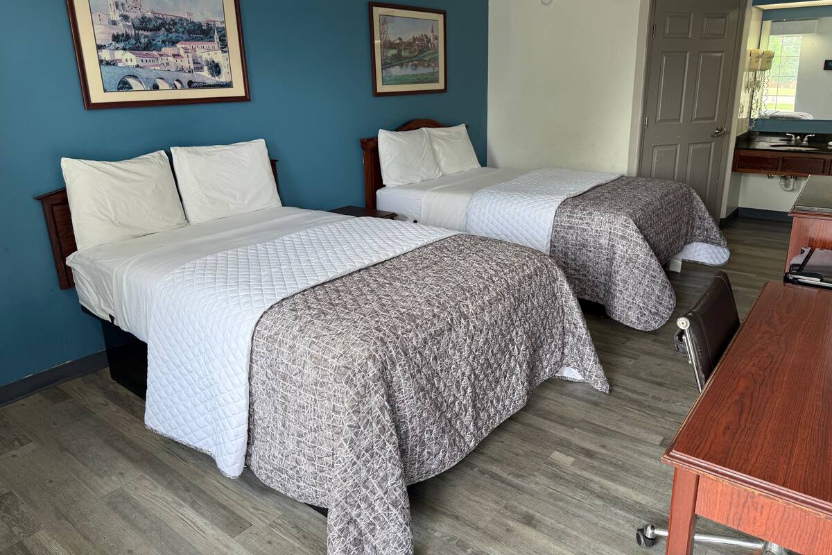 Una habitación de hotel con dos camas, un escritorio de madera y dos cuadros en la pared.