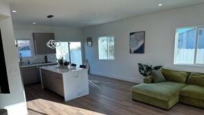A modern kitchen with a marble island, wooden flooring, and a green sofa in a bright living area with large windows. - Charming 2-bedroom apartment with WiFi, AC in beautiful Burbank (Burbank)