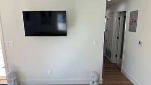 A hallway with a flat-screen TV mounted on the wall, a stone sculpture on the floor, and a door with a red sign. - Charming 2-bedroom apartment with WiFi, AC in beautiful Burbank (Burbank)