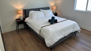A neatly made bed with white linens, two bedside lamps, a modern abstract painting, and a window on the right.