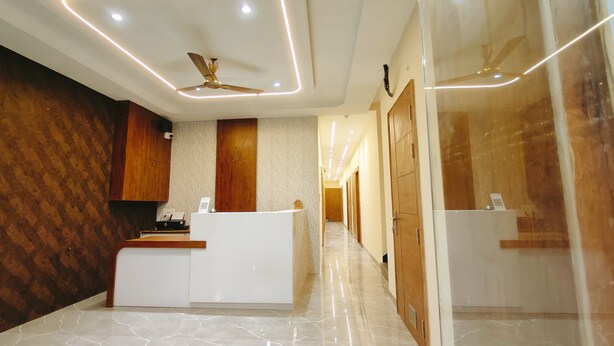 A modern reception area with a marble floor, wooden paneling, a reception desk, and a ceiling fan. - Hotel Babylon Regency  (Mathura)