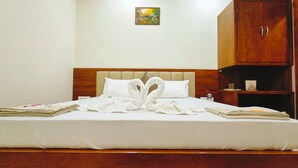 A neatly made bed with towels arranged in a swan shape, a wooden headboard, a small painting on the wall, and a wooden wardrobe. - Hotel Babylon Regency  (Mathura)