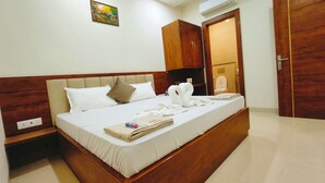A neatly made bed with white linens, a wooden headboard, and a small bedside table with a lamp. - Hotel Babylon Regency  (Mathura)