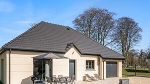 A two-story house with a sloped roof, a patio with outdoor furniture, and a garage. - Gîtes de France® - La Villa Maxence (CRASVILLE LA MALLET)