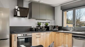 A modern kitchen with wooden cabinets, stainless steel appliances, and a dining area with a table set for two. - Gîtes de France® - La Villa Maxence (CRASVILLE LA MALLET)