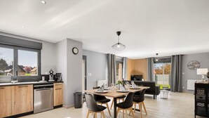 A modern kitchen with wooden cabinets, a dishwasher, and a dining area with a table set for four. - Gîtes de France® - La Villa Maxence (CRASVILLE LA MALLET)
