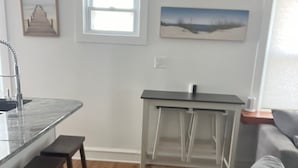 Et moderne køkken med en central ø, træbænke, en grå sofa og kunst på væggene.