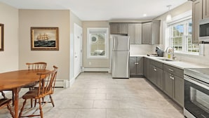 A modern kitchen with a dining area, featuring a large wooden table and chairs, stainless steel appliances, and a view through a window. - Updated & Great Downtown Location, Built 1841 (Salem)