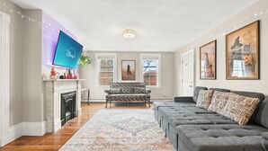 A living room with a fireplace, a grey sofa, a patterned rug, and framed artwork on the walls. - Updated & Great Downtown Location, Built 1841 (Salem)
