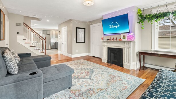 A spacious living room with a grey sectional sofa, a fireplace, a mounted TV displaying Disney+, and a staircase leading to another level. - Updated & Great Downtown Location, Built 1841 (Salem)
