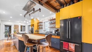 A modern kitchen with a central island, wooden chairs, and a black refrigerator.