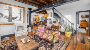 A spacious living room with a wooden ceiling, a colorful patterned sofa, a floral armchair, and a coffee table.
