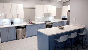 A modern kitchen with white and blue cabinets, stainless steel appliances, and a central island with bar stools. - Awesome Homes - Harbour View (Castries)