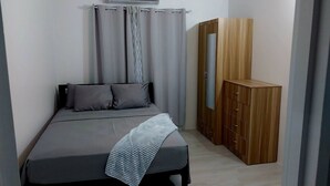 A bedroom with a bed, grey curtains, a wooden wardrobe, and a grey blanket. - Awesome Homes - Harbour View (Castries)