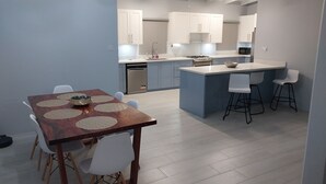 A modern kitchen with a dining area, featuring a wooden table with placemats, white chairs, and a small island with stools. - Awesome Homes - Harbour View (Castries)