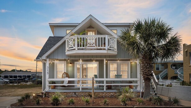 A coastal house with a balcony, a palm tree, and a view of the ocean.