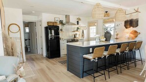 A modern kitchen with a central island, black refrigerator, and wicker bar stools.