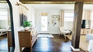 Un dormitorio con piso de madera, un aparador, una silla, un espejo grande y una puerta que da a un balcón.