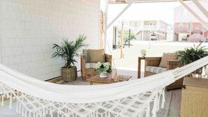 A hammock set up in a covered outdoor area with a wooden table, chairs, and potted plants.