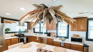 A modern kitchen with wooden cabinets, a white countertop, and a central island with woven placemats and candles. - Hidden gem in Kure|2min walk to Beach|Hot Tub (Kure Beach)