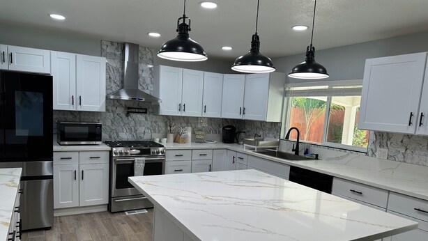 A modern kitchen with white cabinets, a large island, stainless steel appliances, and pendant lighting. - Spacious cozy Oasis retreat with private pool  Backyard (Modesto)