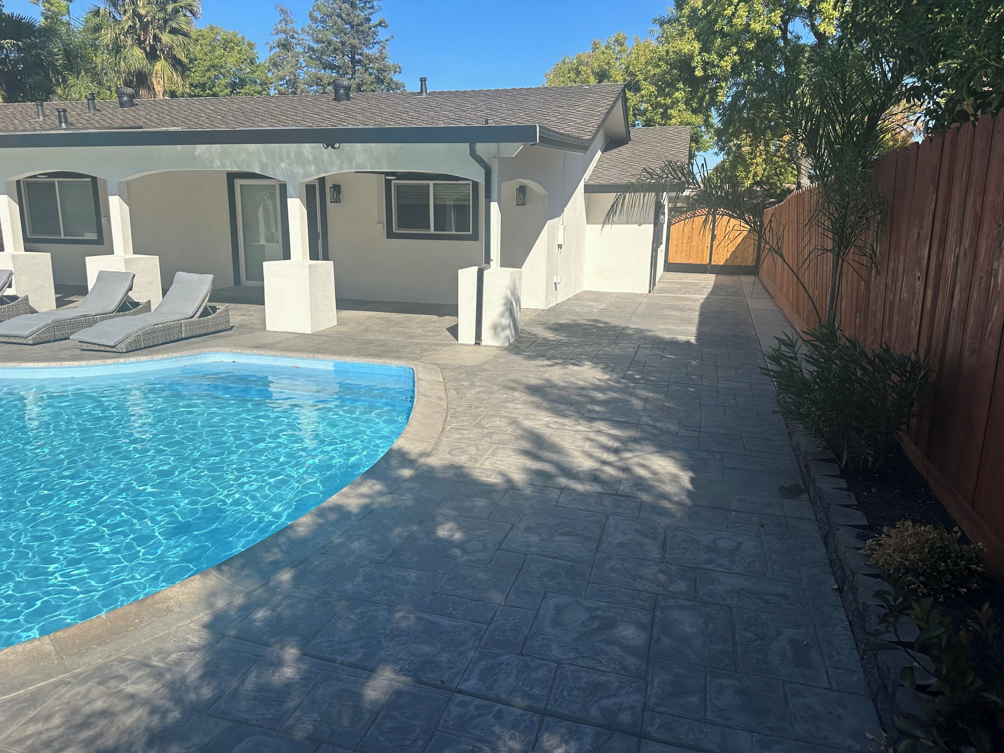A backyard with a swimming pool, lounge chairs, and a wooden fence.