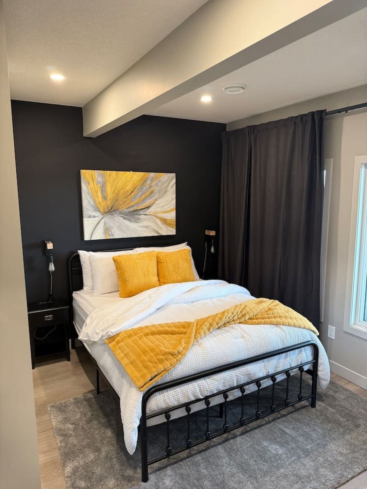 A modern bedroom with a black metal bed frame, white bedding, and a yellow throw blanket.