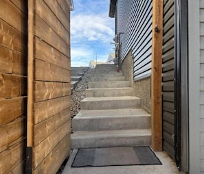 Eine schmale Betontreppe führt zu einem Gebäude, das auf einer Seite Holzverkleidung und auf der anderen Metallverkleidung hat.