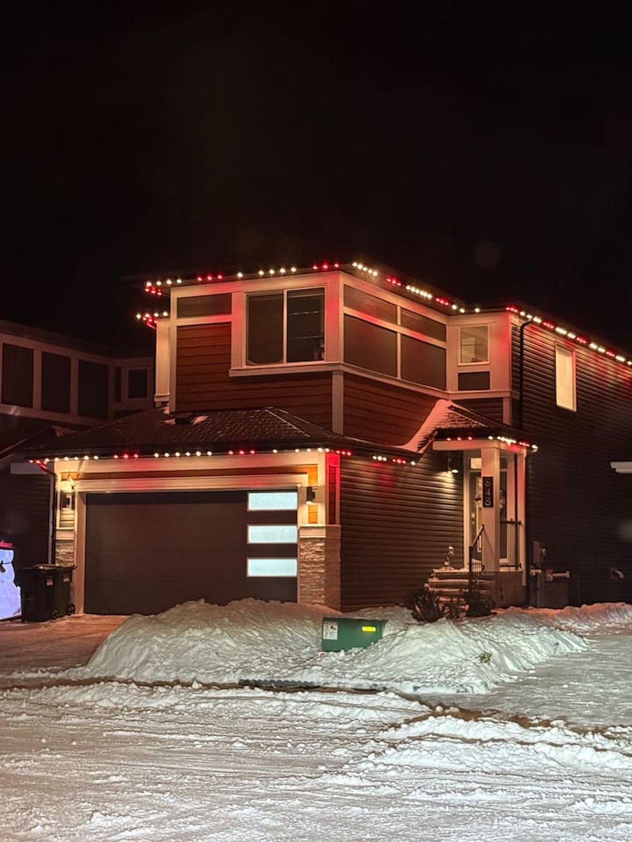 A two-story house with a garage and a covered porch area, surrounded by snow.