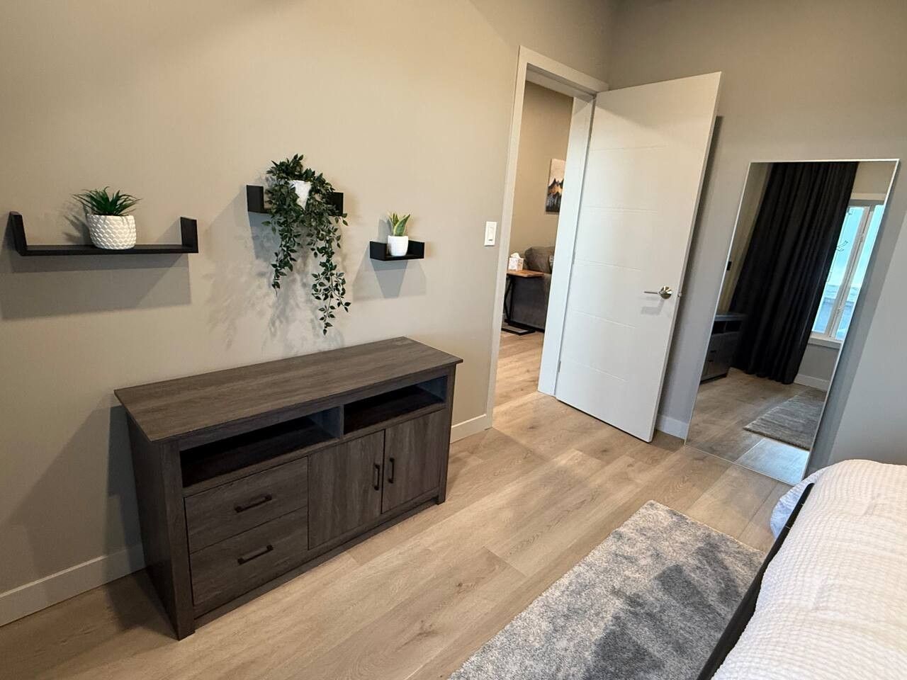 A bedroom with a bed, a wooden dresser, a mirror, and a door leading to another room.