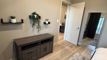 A bedroom with a bed, a wooden dresser, a mirror, and a door leading to another room.