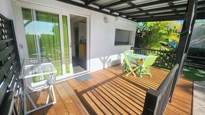 A wooden deck with a table and chairs, a grill, and a sliding glass door leading to a room. - T2 CREOLE apartment by the pool (Sainte-Luce)