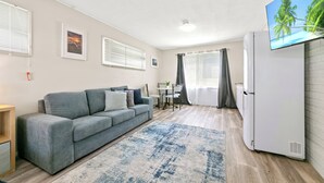 Ein modernes Wohnzimmer mit einem grauen Sofa, einem kleinen Esstisch und einem an der Wand befestigten Fernseher.