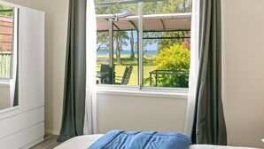 Ein Schlafzimmer mit großem Fenster, einem Bett und Blick auf einen Außenbereich mit Tisch und Stühlen.