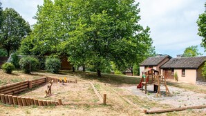 Ein Spielplatz mit Rutsche und Klettergerüsten, umgeben von einem Holzzaun und einem großen Baum.