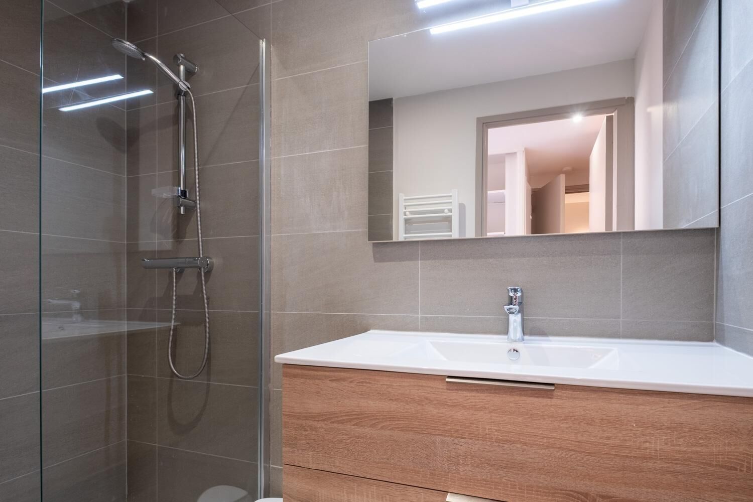 Une salle de bain moderne avec une douche à parois de verre, un lavabo blanc et un meuble-lavabo en bois.