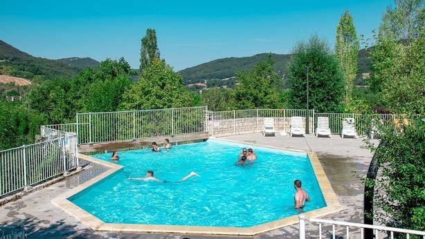 Ein Schwimmbecken, umgeben von einem weißen Zaun, mit mehreren Personen im Wasser.