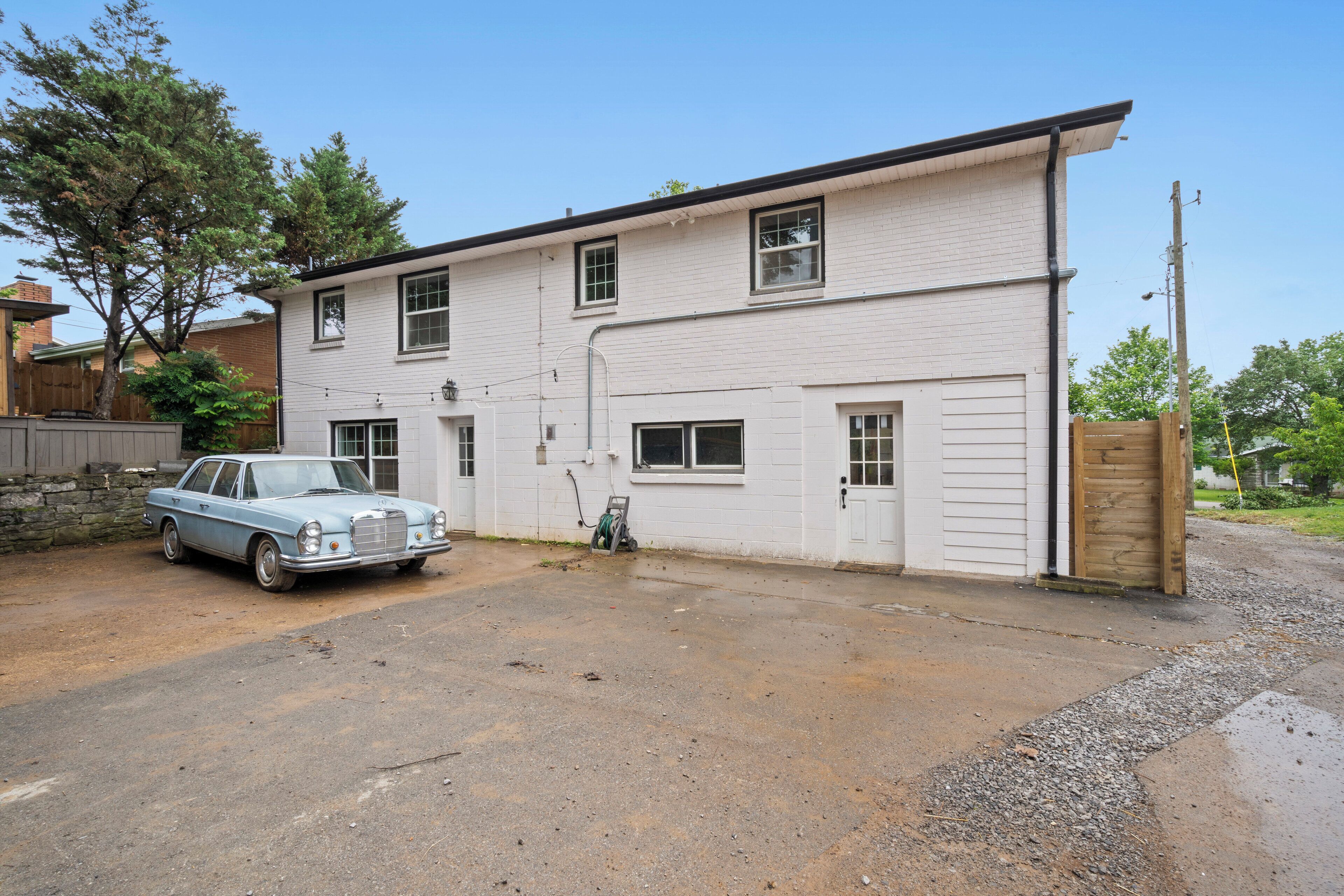 A two-story white building with a garage, a parked vintage car, and a wooden fence.
