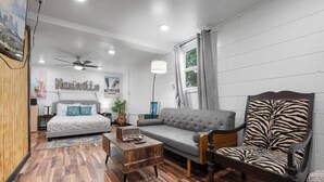 A modern living room with a bed, a grey sofa, a zebra-patterned chair, a wooden coffee table, and a ceiling fan. - Charming 5bd/4ba 15mi BNA 7mi Broadway 6mi Vandy (Nashville)