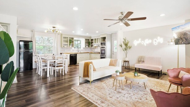 A modern kitchen with white cabinets, a dining area with a white table and chairs, a living room with a white sofa and pink chairs, and a ceiling fan. - Charming 5bd/4ba 15mi BNA 7mi Broadway 6mi Vandy (Nashville)