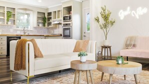 A modern living room with a white sofa, round wooden coffee table, and a kitchen in the background. - Charming 5bd/4ba 15mi BNA 7mi Broadway 6mi Vandy (Nashville)