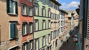 Una hilera de edificios coloridos de varios pisos con balcones, una calle adoquinada y peatones.