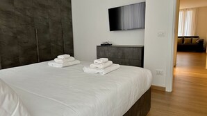Una habitación de hotel moderna con una cama grande, un televisor de pantalla plana montado en la pared y suelo de madera.