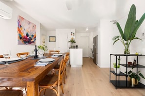 A modern kitchen with a wooden dining table, chairs, and a black shelving unit with plants. - Walking Distance to Darling Harbour (Sydney)