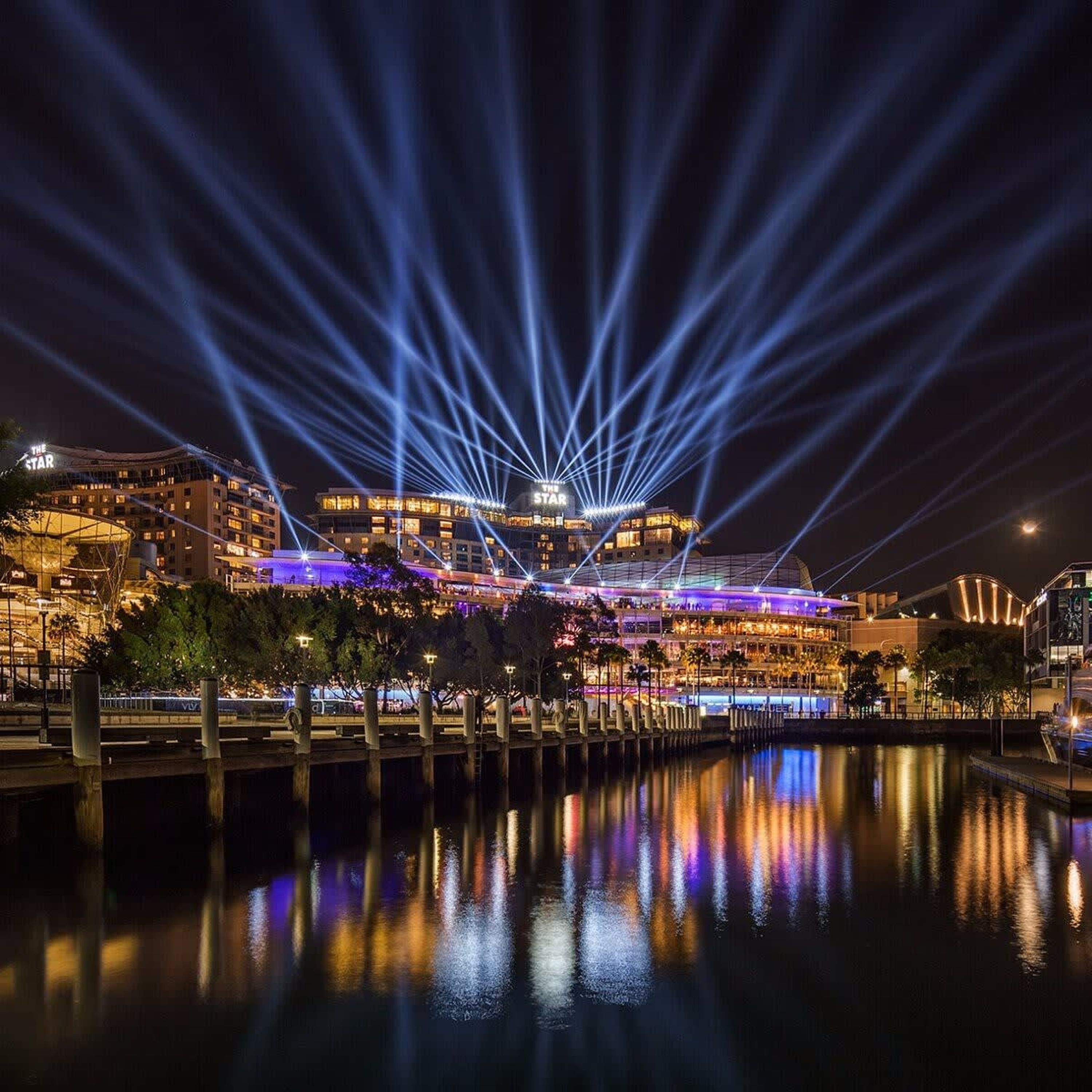 Ein Hotel am Wasser mit einem gut sichtbaren Schild 'The Star', das Lichter im Wasser reflektiert, und einem modernen architektonischen Design mit mehreren Etagen und Balkonen.