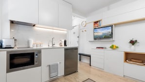 A modern kitchen with white cabinets, a built-in microwave, and a dishwasher. There's a clock on the wall and a TV mounted above the counter. - Bay View in Rushcutters Bay (Sydney)